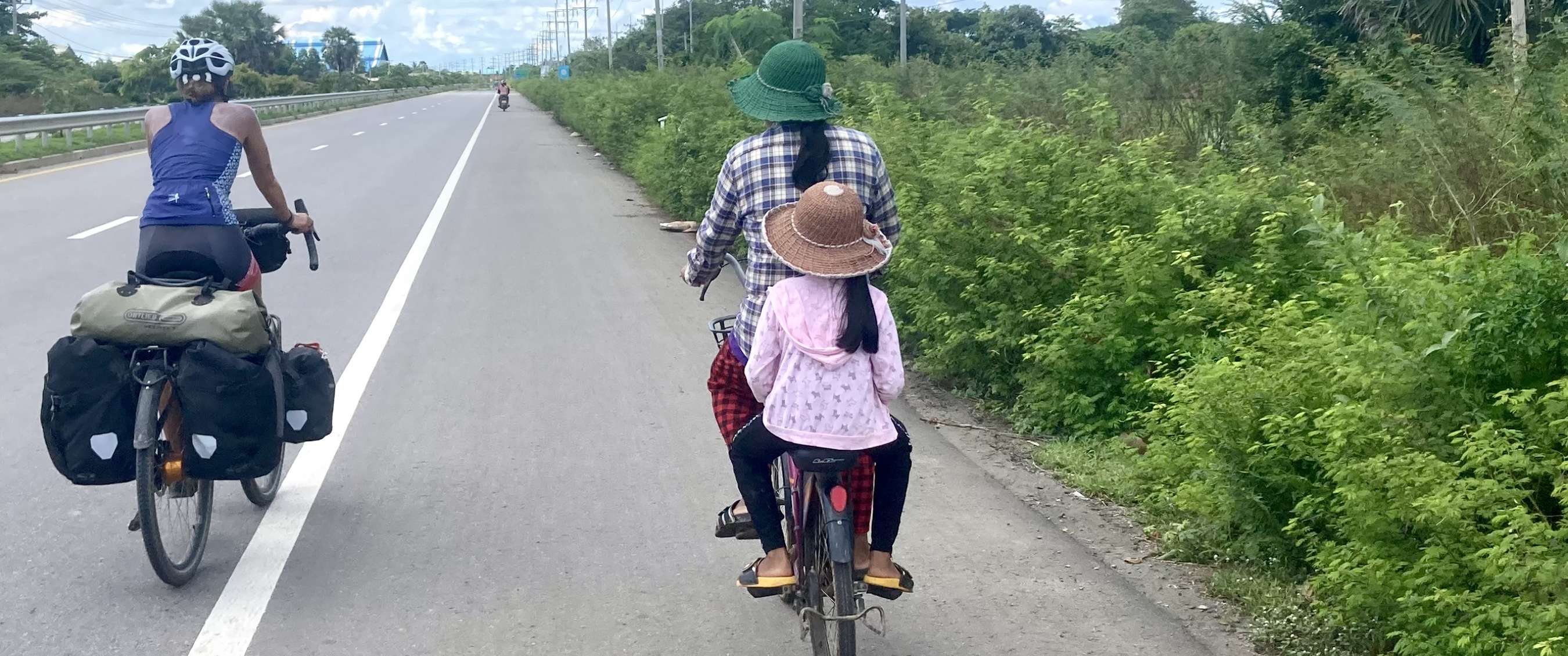 Cyclotouriste avec bagages roule sur une route calme en Asie à côté d’une femme avec un enfant à l’arrière de son vélo.