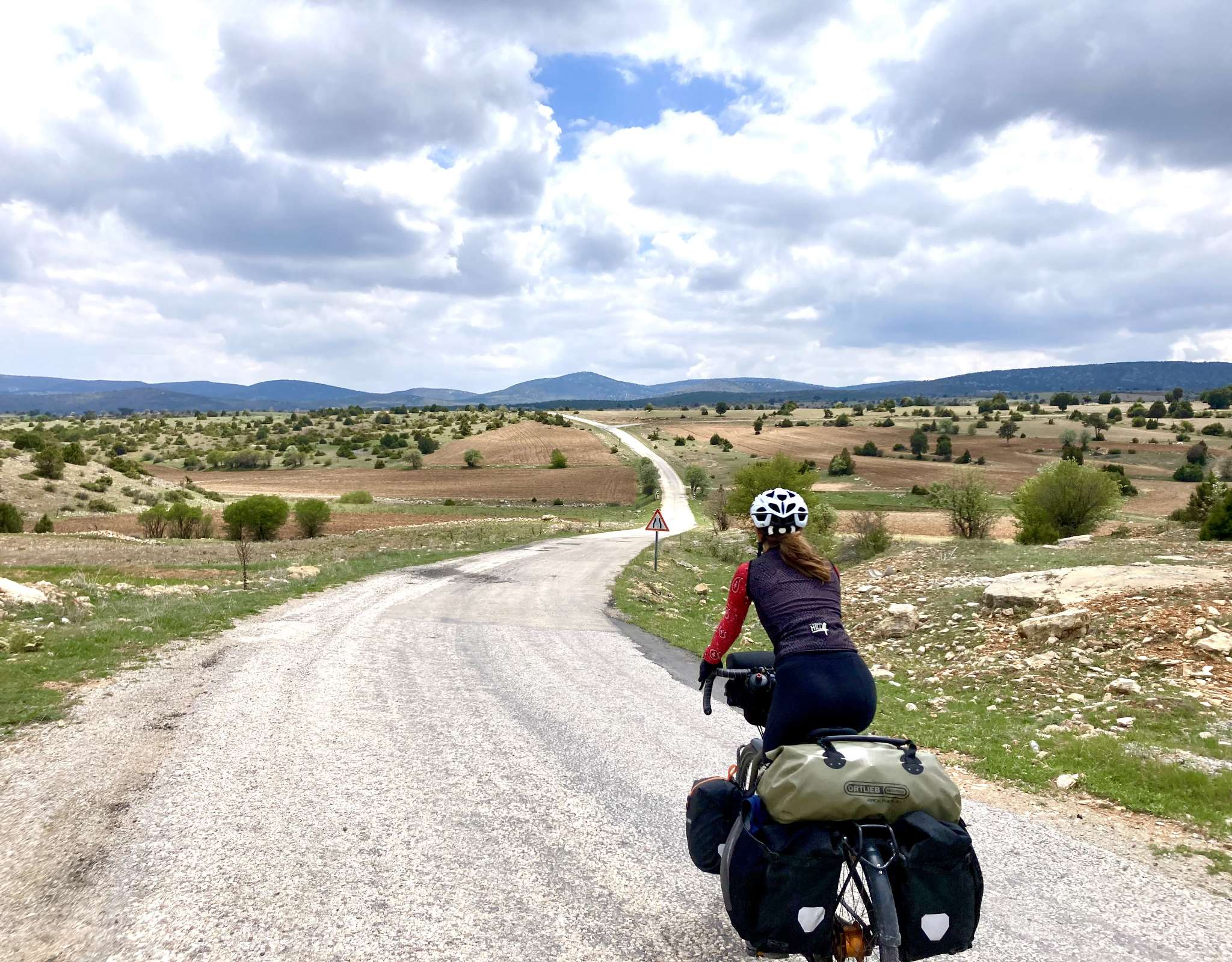 Marie, chargée de bagages, contemple une route sinueuse traversant un paysage vallonné.